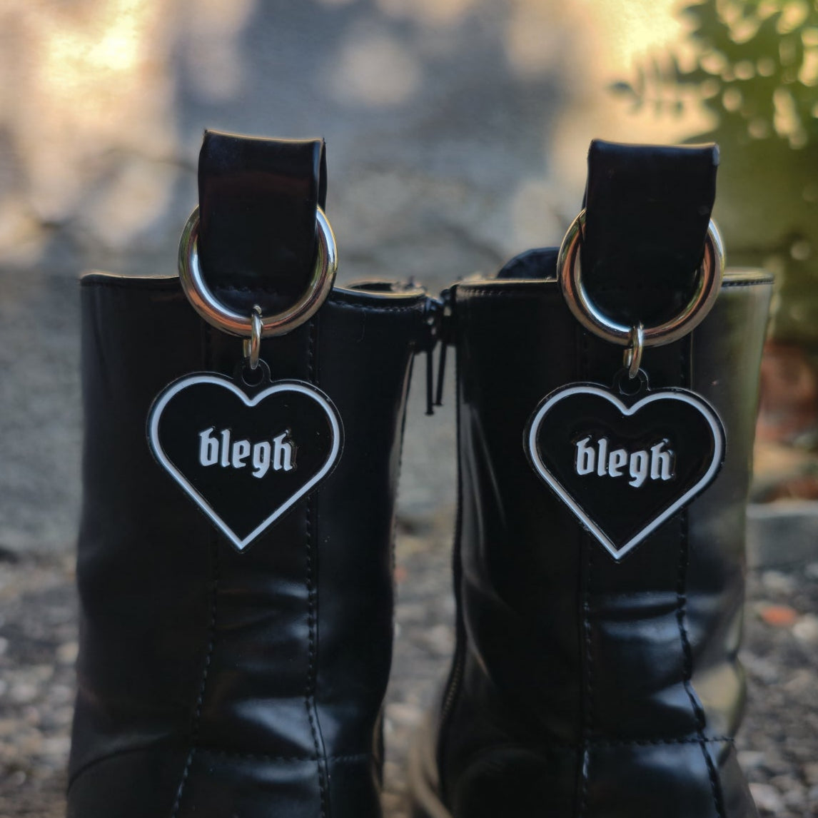 Schwarzer Boot Charm in Herzform mit weißer Umrandung und dem Wort „blegh“, befestigt an einem silbernen Karabiner für die Zuglasche von Stiefeln.