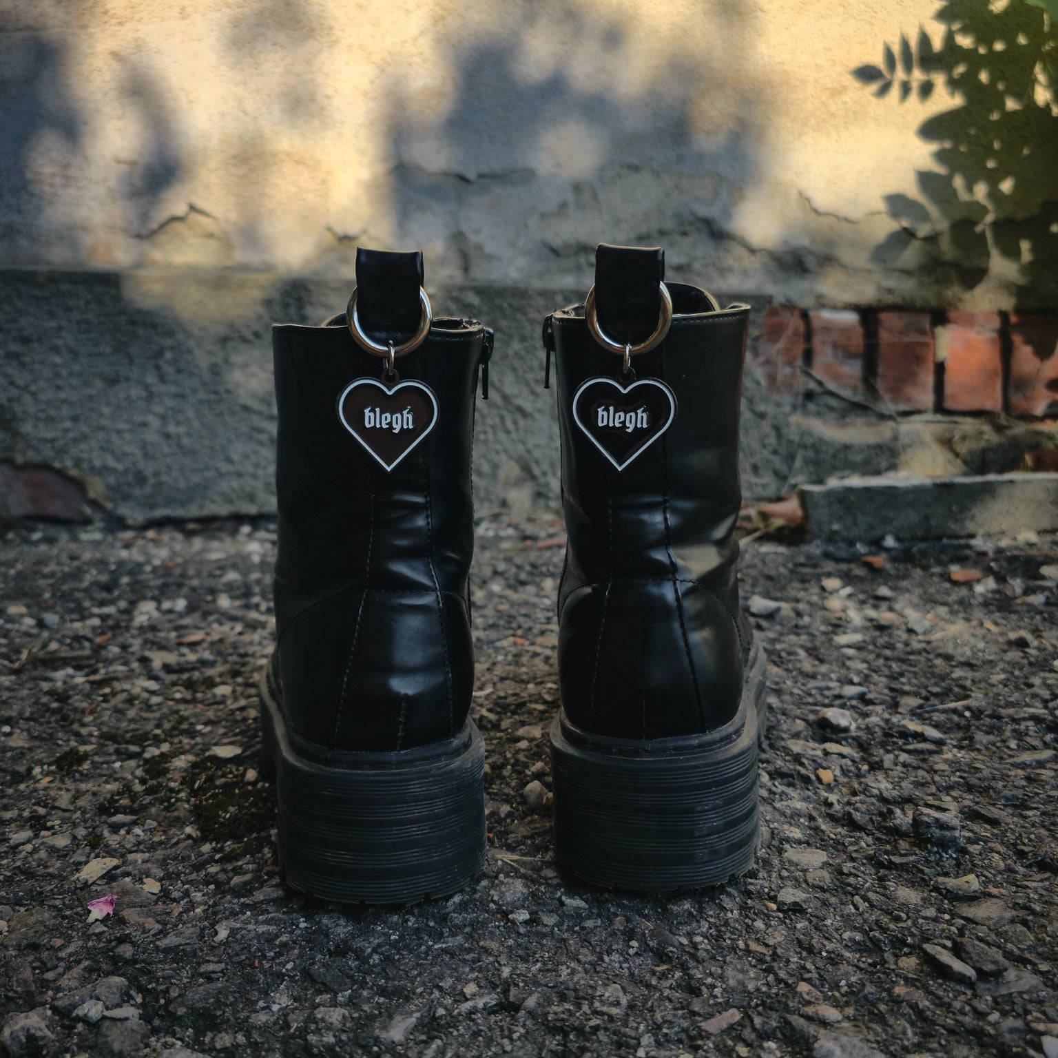 Schwarzer Boot Charm Stiefelanhänger in Herzform mit weißer Umrandung und dem Wort „blegh“, befestigt an einem silbernen Karabiner für die Zuglasche von Stiefeln.