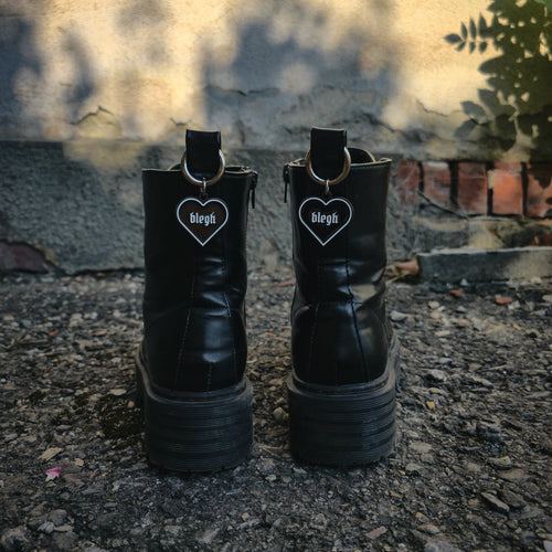Schwarzer Boot Charm Stiefelanhänger in Herzform mit weißer Umrandung und dem Wort „blegh“, befestigt an einem silbernen Karabiner für die Zuglasche von Stiefeln.