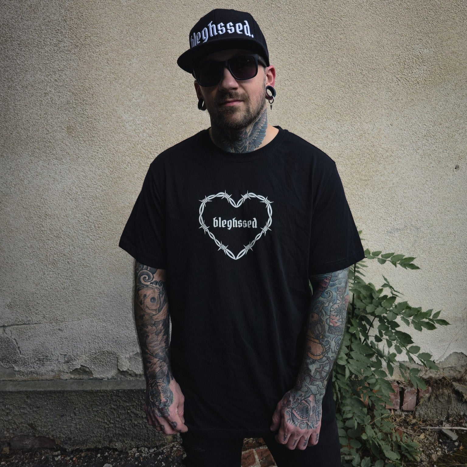 Schwarzes Shirt mit „bleghssed“-Print in einem Herz aus Stacheldraht, getragen von vorne fotografiert.